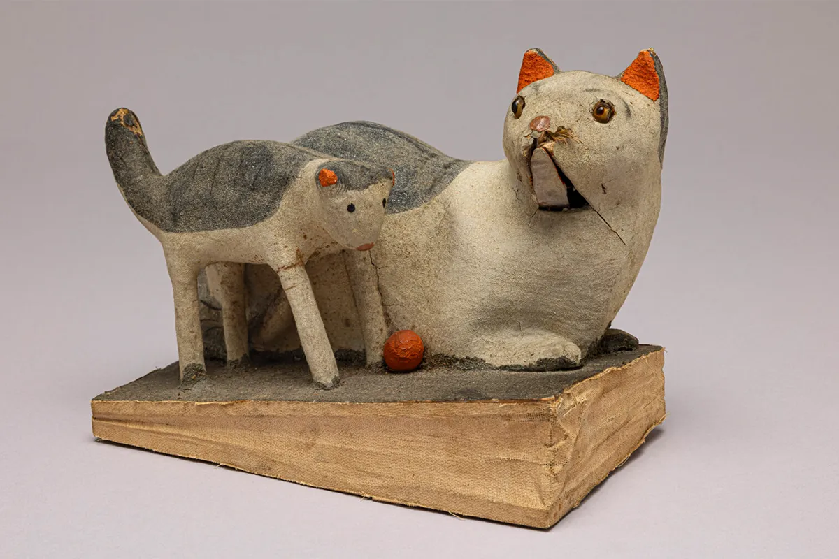 Vintage papier-mâché toy cat with kitten from Russia, around 1900, displayed on a fabric-covered base.