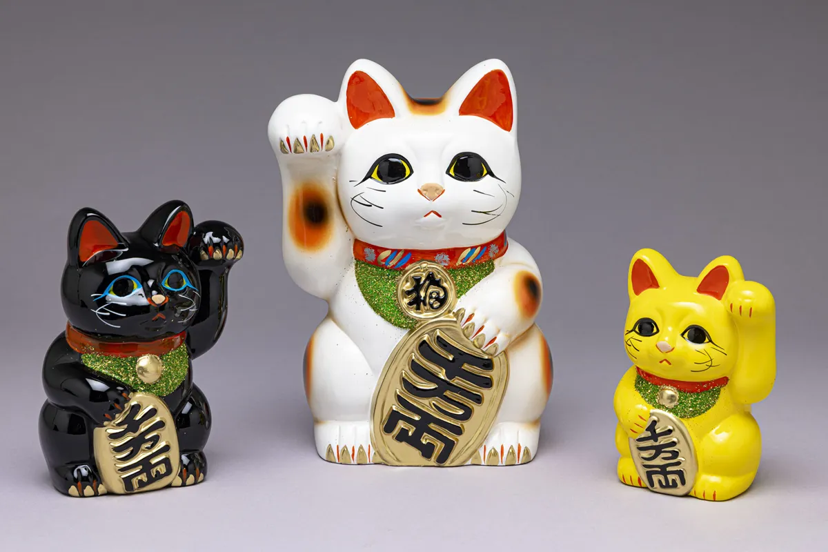 Three ceramic Maneki-neko (beckoning cat) figures in black, white, and yellow, from Tokoname, Japan.