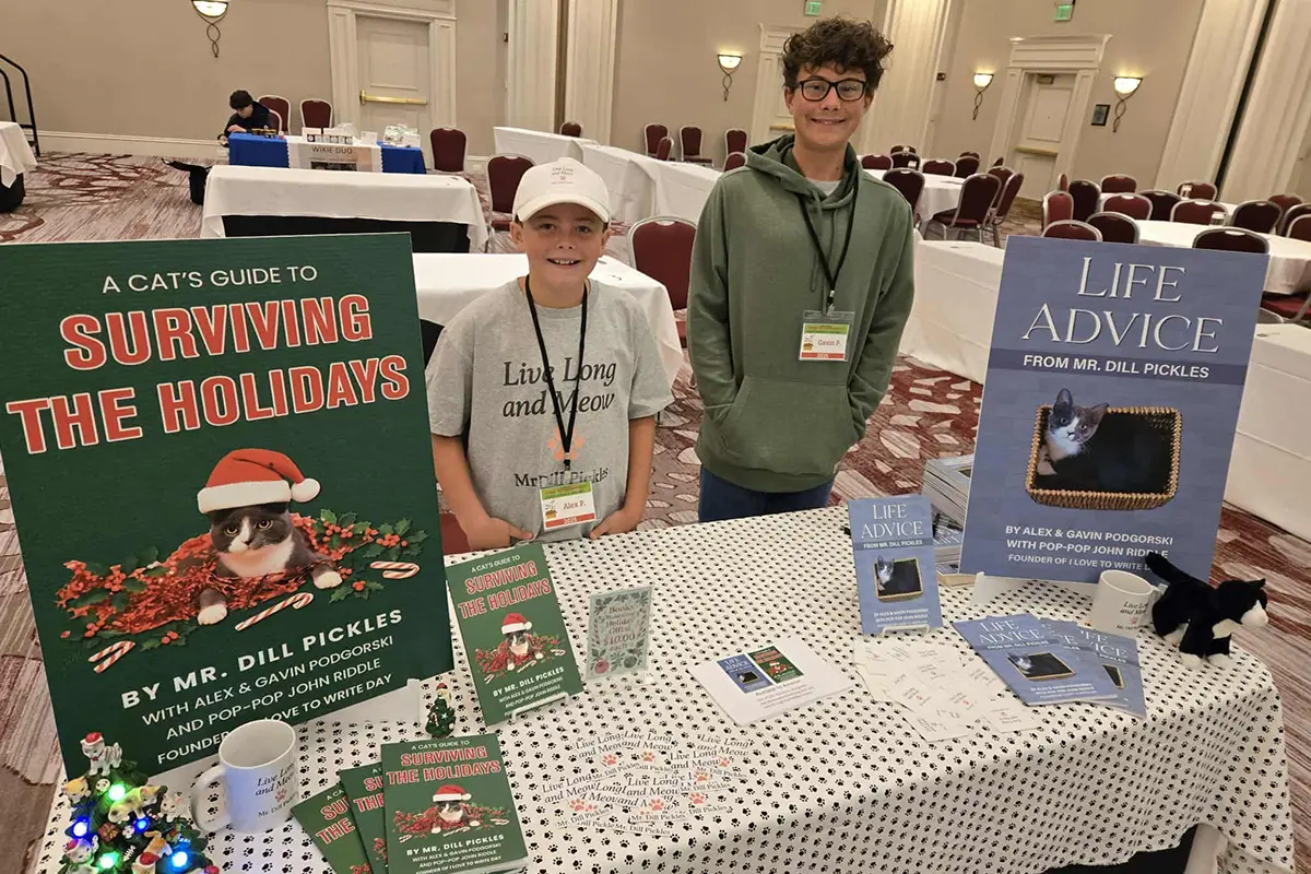 Alex and Gavin Podgorski smiling behind a display of Mr. Dill Pickles’ funny cat books at the Kid Entrepreneur Expo in Virginia.