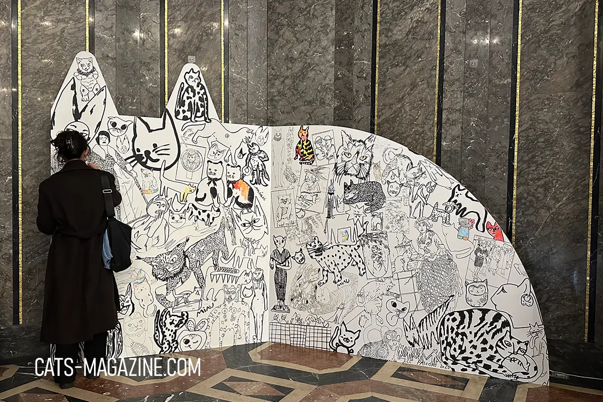 Visitor standing beside a large illustrated cat mural covered in artistic cat drawings at the CATS exhibition Hamburg.