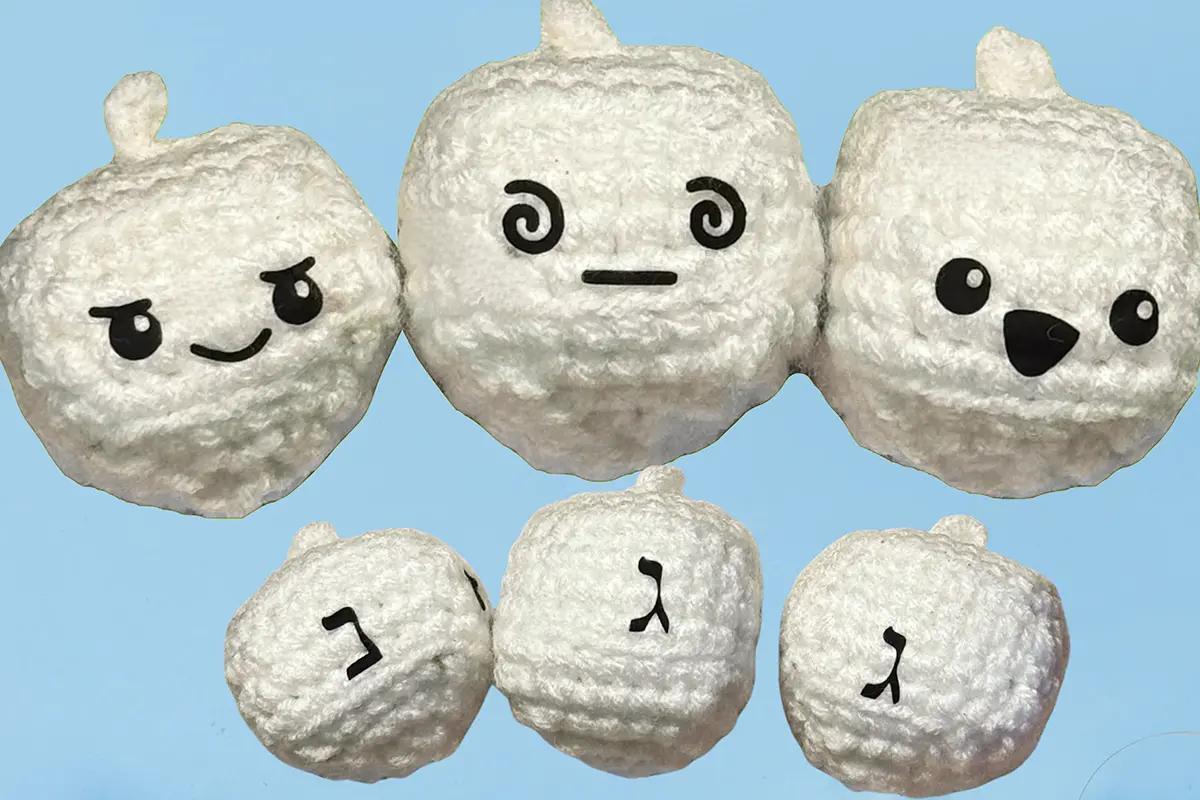 Group of white crocheted dreidel-themed Chunkles cat toys with expressive faces on a light blue winter background.