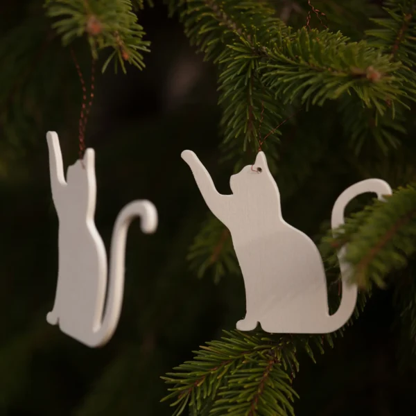 Zen Cat Wooden Ornaments – Minimalist Pair Two minimalist wooden cat ornaments hanging on evergreen branches