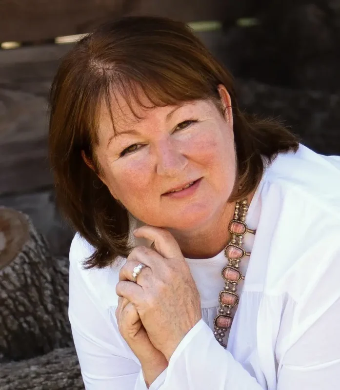 Children’s author Cindy J. Vanous smiling in a white blouse, with her hands beneath her chin.